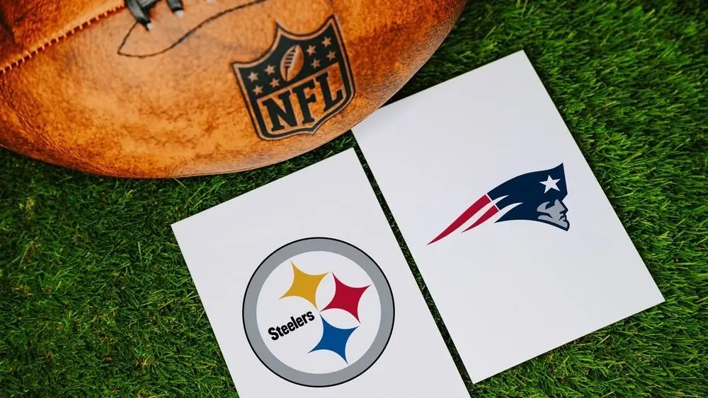 Pittsburgh Steelers vs New England Patriots NFL match concept featuring team logos printed on white paper next to a leather football on green turf. PENNSYLVANIA^ USA^ SEPTEMBER 7^ 2026