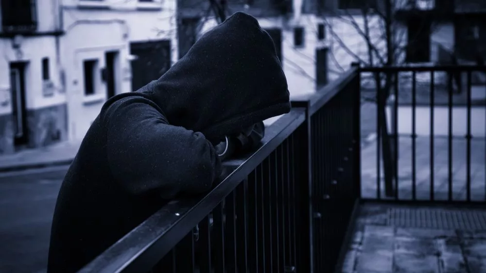 silhouette of man in dark hoodie outside leaning on fence