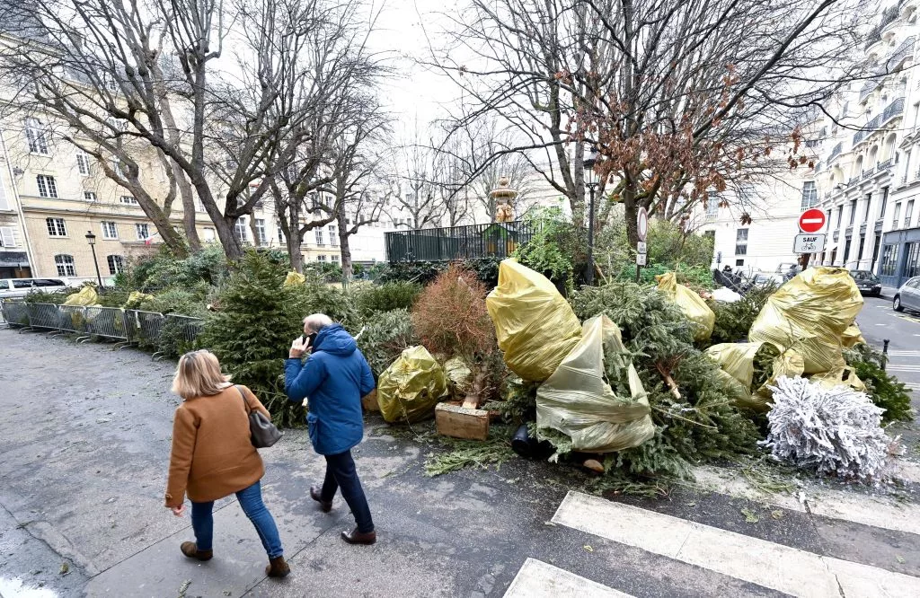 Pedestrians walk past a recycle collected point for Christmas trees, in Paris, on January 8, 2023. - Around 190 collection points are available in Paris to drop off natural Christmas trees. (Photo by Stefano RELLANDINI / AFP) (Photo by STEFANO RELLANDINI/AFP via Getty Images)