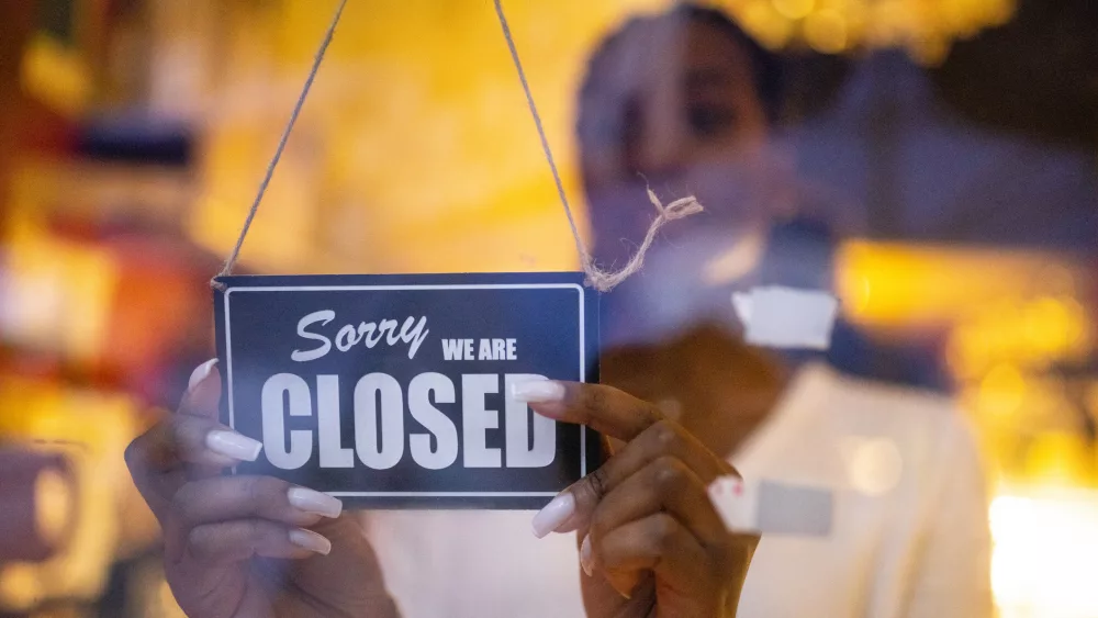 Woman putting closed sign on glass front door of coffee shop. Small business closed for covid-19 lockdown