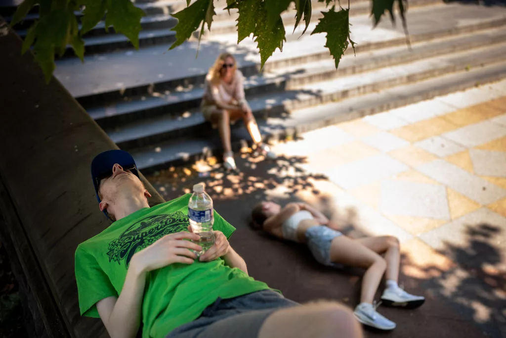 WASHINGTON, DC - JUNE 21: Vicki McCormick (C) and her children Louis and Rosa, visiting from Kirkcaldy, Scotland, rest in the shade on the West Lawn of the U.S. Capitol Building as much of the Northeast braces for a heat wave on June 21, 2024 in Washington, DC. Temperatures are forecasted to soar into the high 90s, with a heat index surpassing 100 degrees. (Photo by Andrew Harnik/Getty Images)