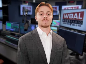 WBAL NewsRadio's Nick Testoni, reporter and host of Saturday's talk show, Sportsline. Nick stands in the WBAL Radio studio in a sports jacket with a straight face.