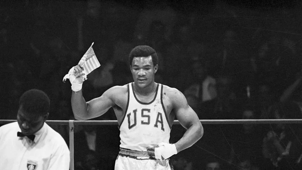 (Original Caption) 10/26/1968-Mexico City, Mexico- George Foreman of Houston, TX, waves a small American flag after he won the Olympics heavyweight boxing gold medal to climax America's greatest effort at an Olympics. The US walked away with 45 gold medals, 27 silvers and 34 bronze. Foreman scored a second-round technical knockout over Ionas Chepulis of the Soviet Union.