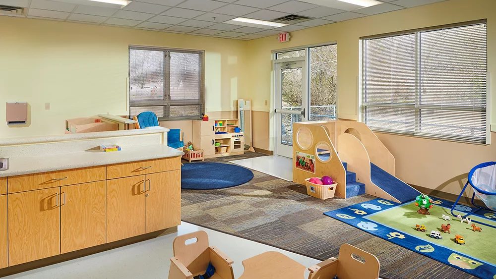 Child care room with chairs, table, cabinet, toys.