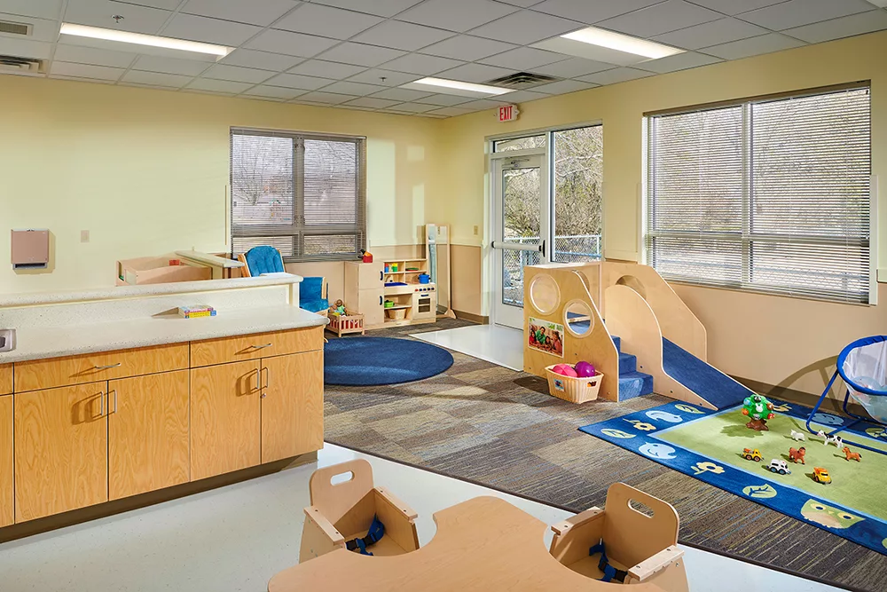 Child care room with chairs, table, cabinet, toys.