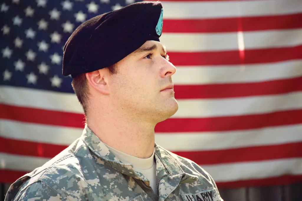 man-wearing-combat-hat-and-top-looking-up-near-flag-of-1202726
