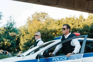 selective-focus-of-mature-policeman-in-sunglasses-and-bulletproof-vests-standing-near-car-at-city