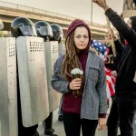 woman-between-displeased-crowd-and-riot-police