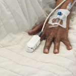 hand-of-african-american-senior-female-patient-lying-in-bed-in-sunny-hospital-room-medicine-healthcare-and-medical-services-unaltered