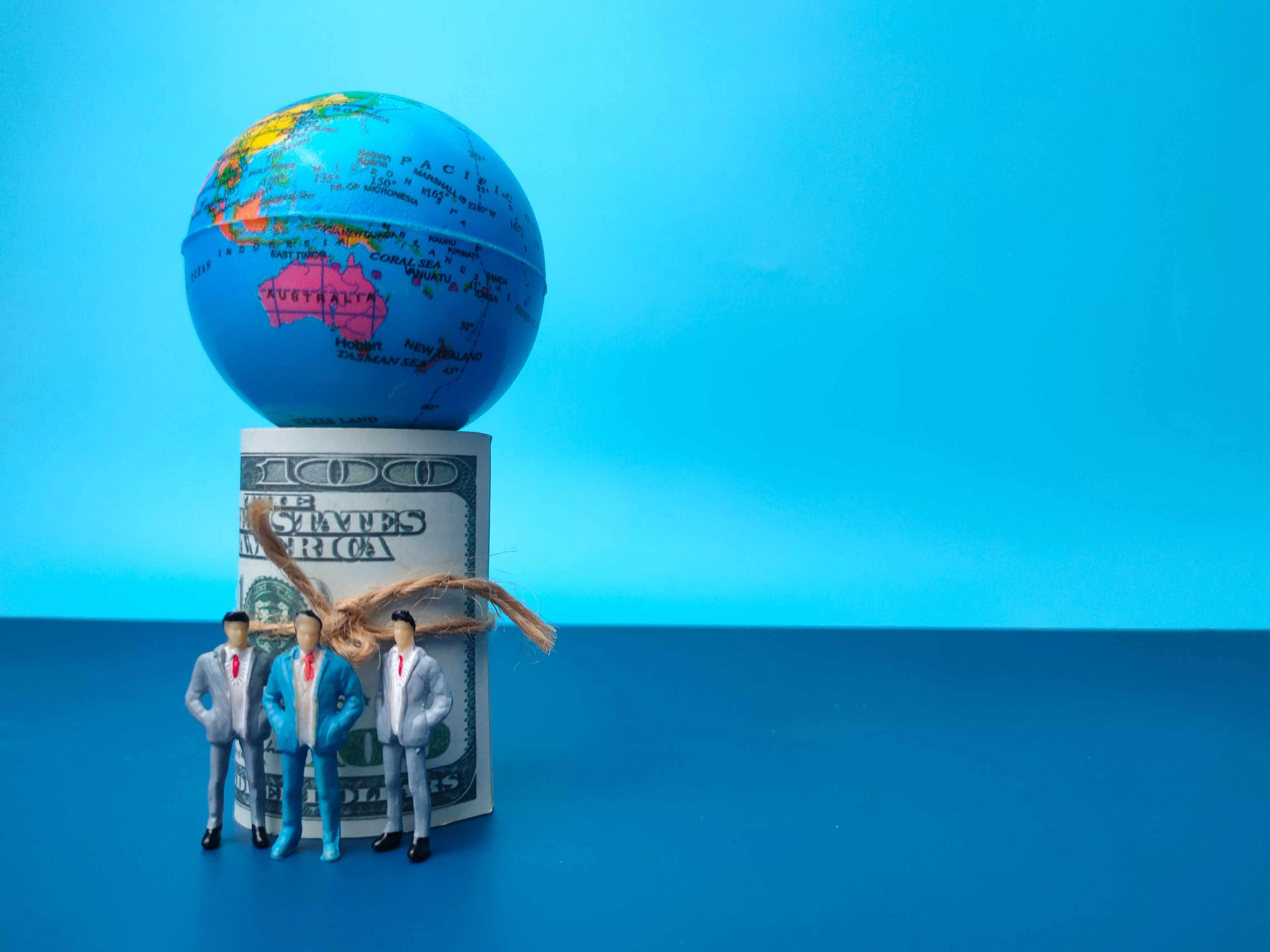 banknotes-globe-and-miniature-people-on-a-blue-bac-2024-12-08-00-12-19-utc