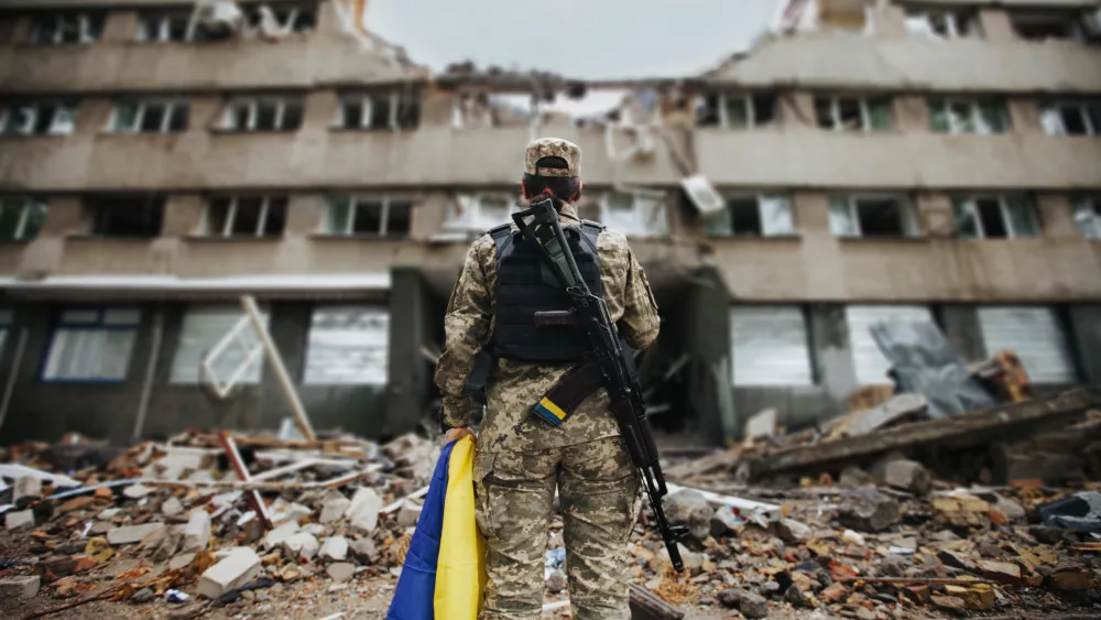 ukrainian-military-woman-with-the-ukrainian-flag-in-her-hands-on-the-background-of-an-exploded-house