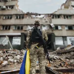 ukrainian-military-woman-with-the-ukrainian-flag-in-her-hands-on-the-background-of-an-exploded-house