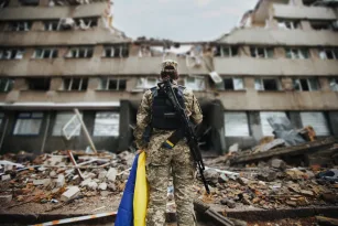 ukrainian-military-woman-with-the-ukrainian-flag-in-her-hands-on-the-background-of-an-exploded-house
