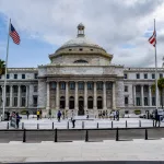 the-front-entrance-of-a-building-with-some-columns-and-two-flags-on-poles