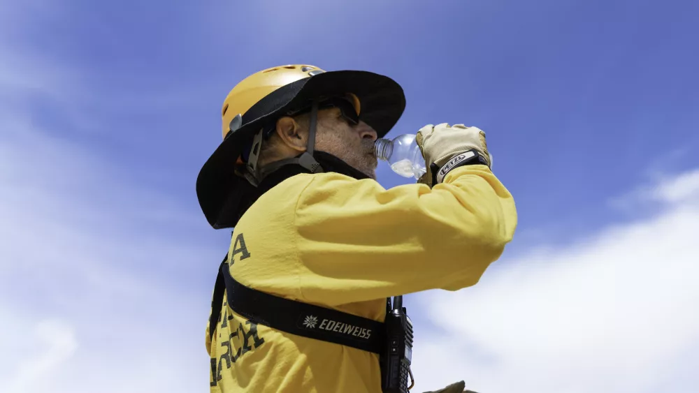 A Joshua Tree Search and Rescue member in a yellow shirt stays hydrated in the summer heat by drinking water