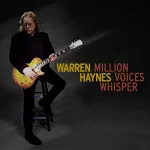 Warren Haynes wearing all black sitting on a stoll