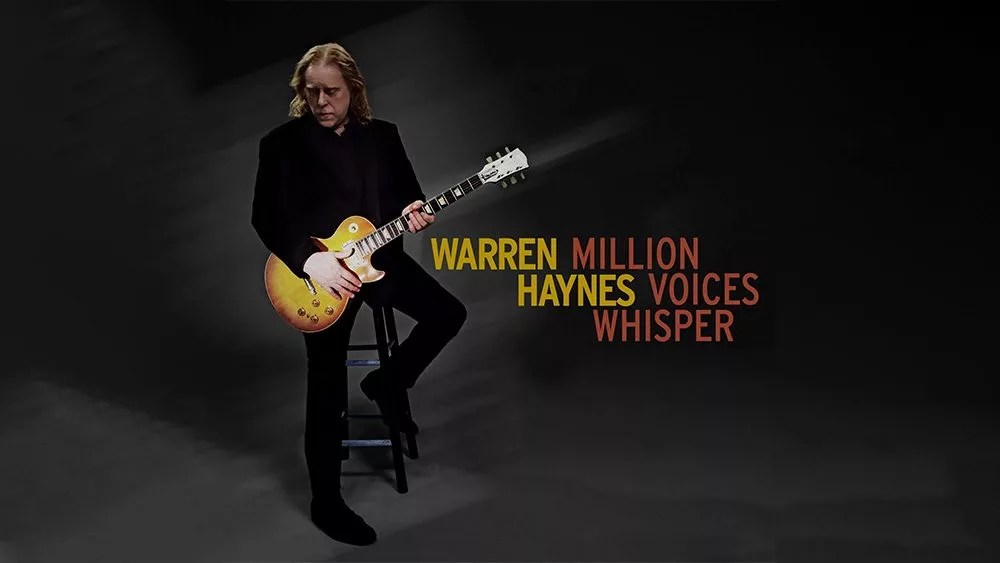 Warren Haynes wearing all black sitting on a stoll