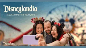Promotional graphic for a Disneyland Resort giveaway. A smiling family of three wearing Mickey and Minnie ears takes a selfie in front of a colorful Disneyland background with a Ferris wheel. Spanish headline reads, “Podrías ganar una visita a Disneylandia de parte de KXYZ.” Below, Spanish text explains the chance to win a family trip to Disneyland Resort, encouraging listeners of La Caliente 92.1 to visit the website and listen for a cue to register. Disneyland logo and legal disclaimer text appear at the bottom.