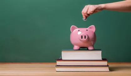 person-depositing-money-in-a-piggy-bank-on-top-of-books-with-chalkboard-3