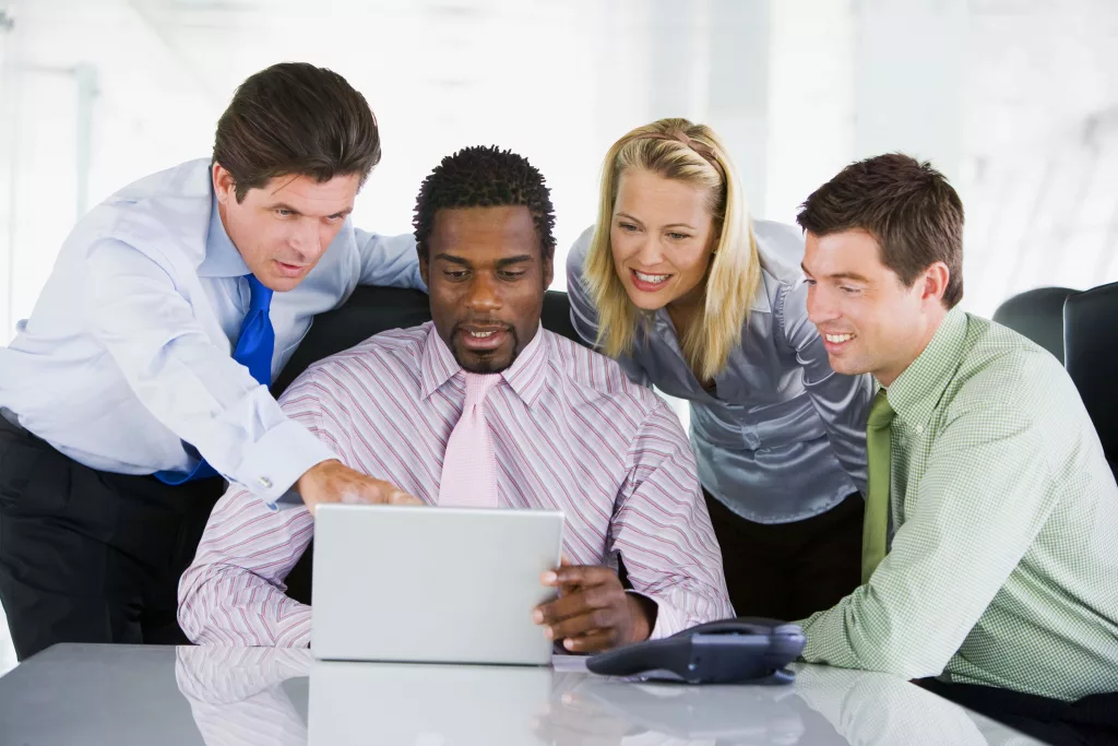 four-businesspeople-in-a-boardroom-pointing-at-laptop-and-smilin