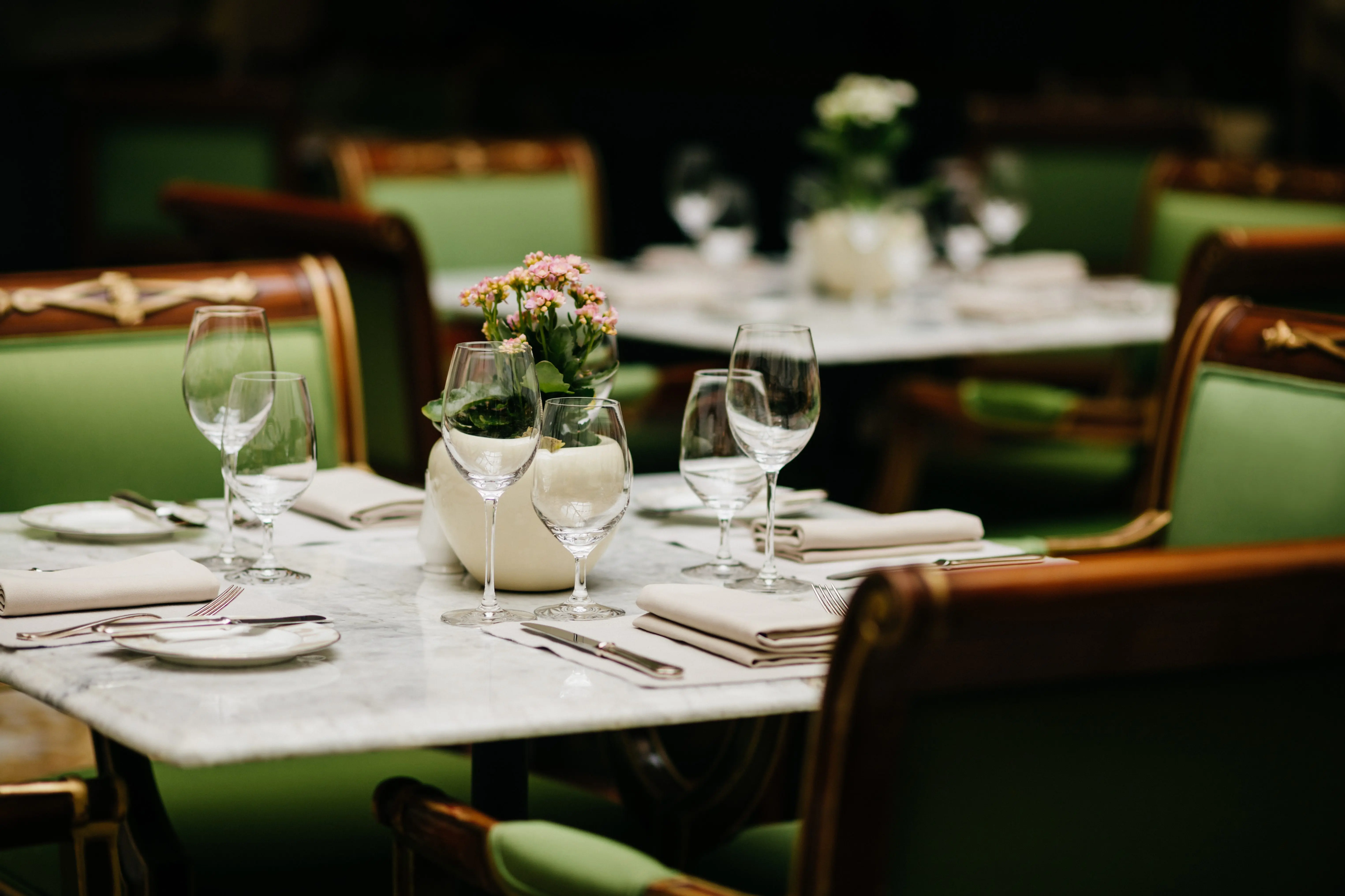 horizontal-shot-of-square-table-served-with-empty-glasses-napkins-plates-forks-and-knives-with-no-dish-green-chairs-around-cozy-restaurant-or-cafe