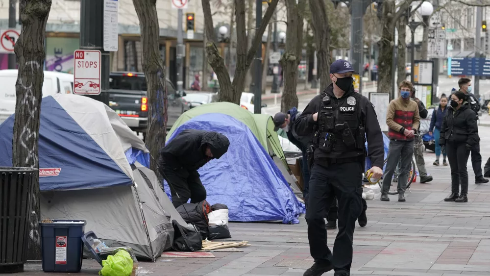 FILE - A Seattle police officer walks past tents used by people experiencing homelessness, March 11, 2022, during the clearing and removal an encampment in Westlake Park in downtown Seattle. Five major U.S. cities, including Seattle, and the state of California will receive federal help to get unsheltered residents into permanent housing under a new plan announced Thursday, May 18, 2023, as part of the Biden administration's larger goal to reduce homelessness 25% by 2025. (AP Photo/Ted S. Warren, File)