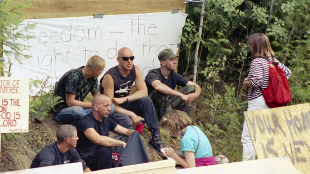 A group of neo-Nazi skinheads sit in the middle of protest signs as they are interviewed near Naples, Idaho on August 28, 1992, where federal authorities continue a standoff with fugitive Randy Weaver nearby. Some area residents are upset with outsiders joining the crowd to support Weaver and making the community appear to be a haven for extremists. (AP Photo/Gary Stewart)