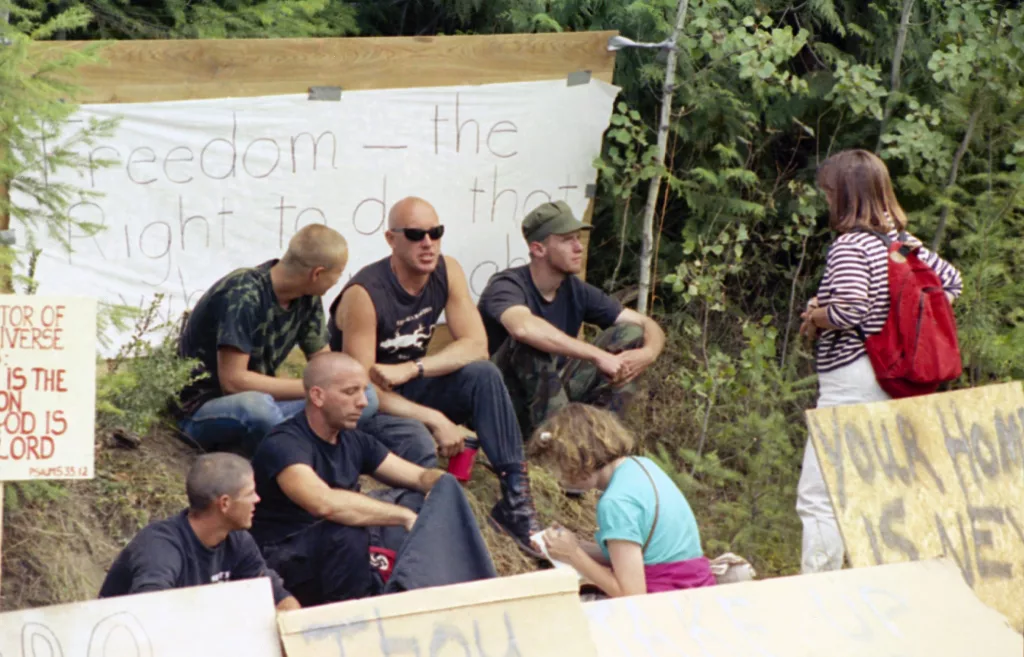 A group of neo-Nazi skinheads sit in the middle of protest signs as they are interviewed near Naples, Idaho on August 28, 1992, where federal authorities continue a standoff with fugitive Randy Weaver nearby. Some area residents are upset with outsiders joining the crowd to support Weaver and making the community appear to be a haven for extremists. (AP Photo/Gary Stewart)