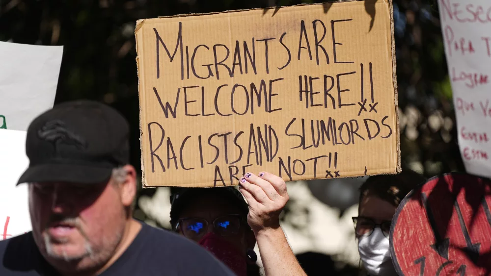 A protester holds up a placard during a rally staged by the East Colfax Community Collective to address chronic problems in the apartment buildings occupied by people displaced from their home countries in central and South America Tuesday, Sept. 3, 2024, in Aurora, Colo. (AP Photo/David Zalubowski)