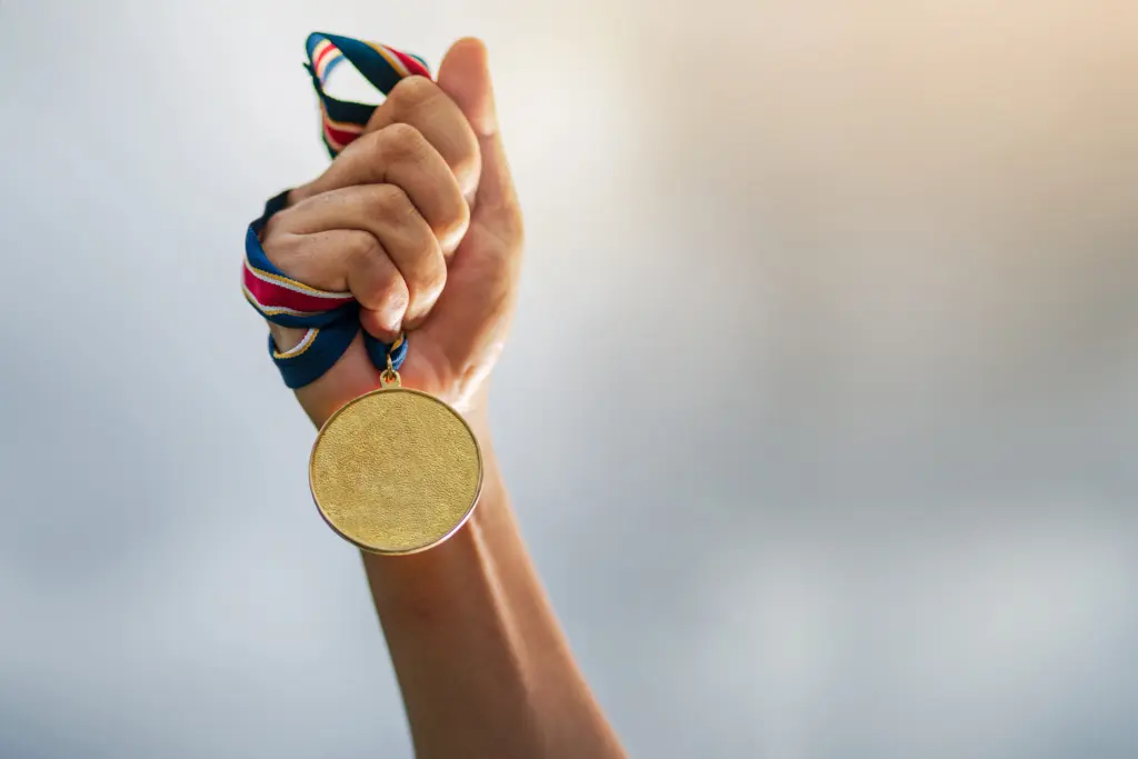 hand-holding-gold-medal-on-sky-background