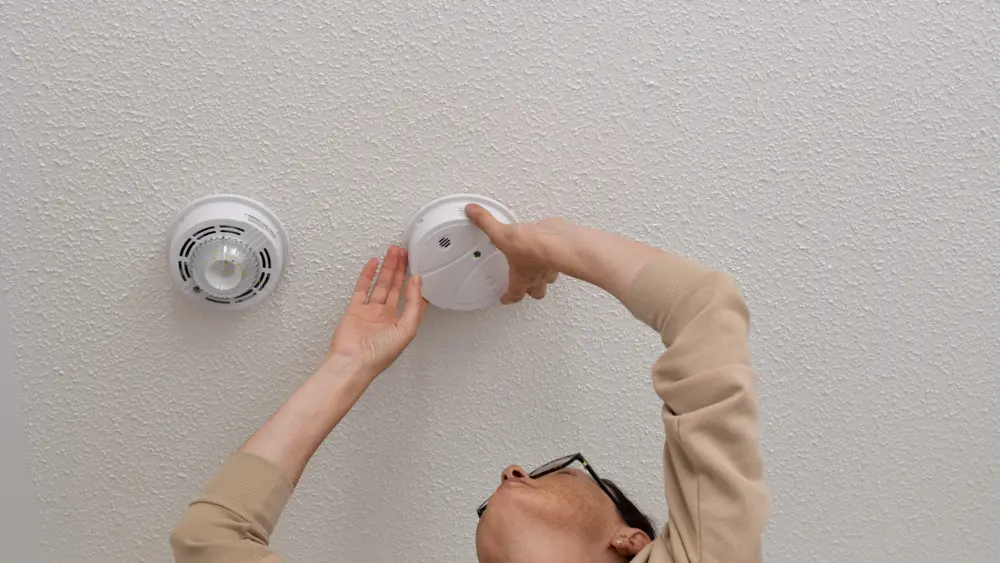 woman-reaching-up-for-smoke-alarm-on-ceiling-at-home