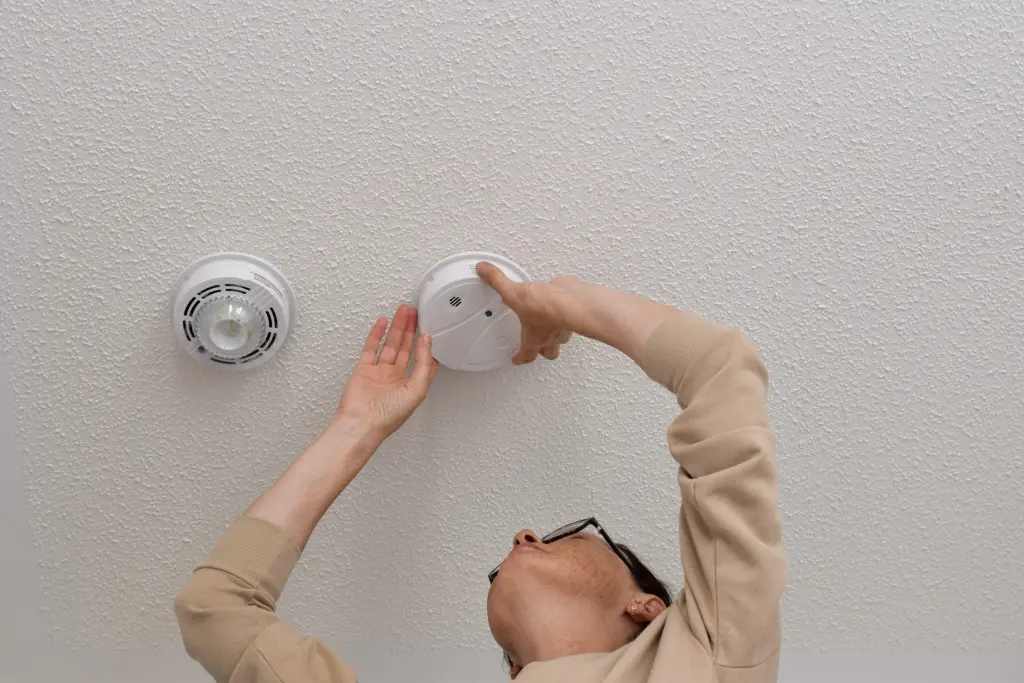 woman-reaching-up-for-smoke-alarm-on-ceiling-at-home