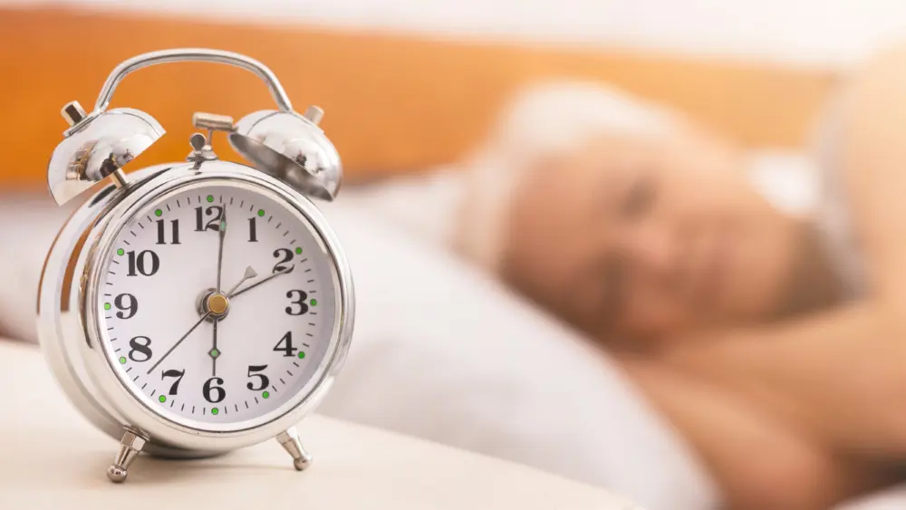 alarm-clock-on-bed-over-sleeping-senior-woman