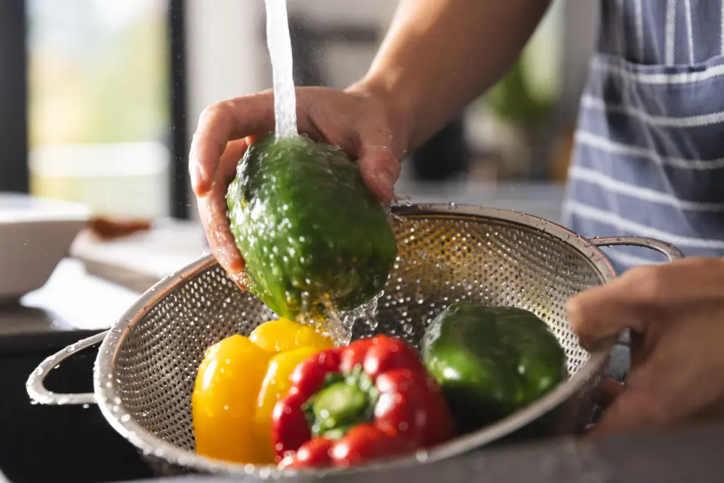 midsection-of-biracial-man-in-apron-washing-peppers-in-kitchen-sink-food-cooking-healthy-lifestyle-and-domestic-life