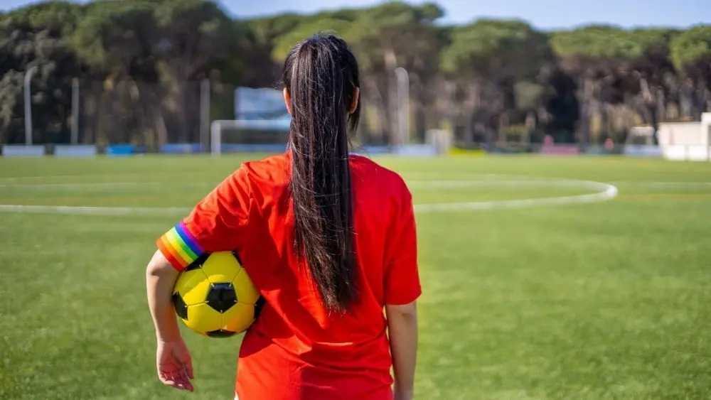 Female soccer player wearing a captain armband with the LGBT pride flag on the field. Campaign against homophobia in football. LGBTQ people in sport concept. Women's Football. Gay pride day and month.