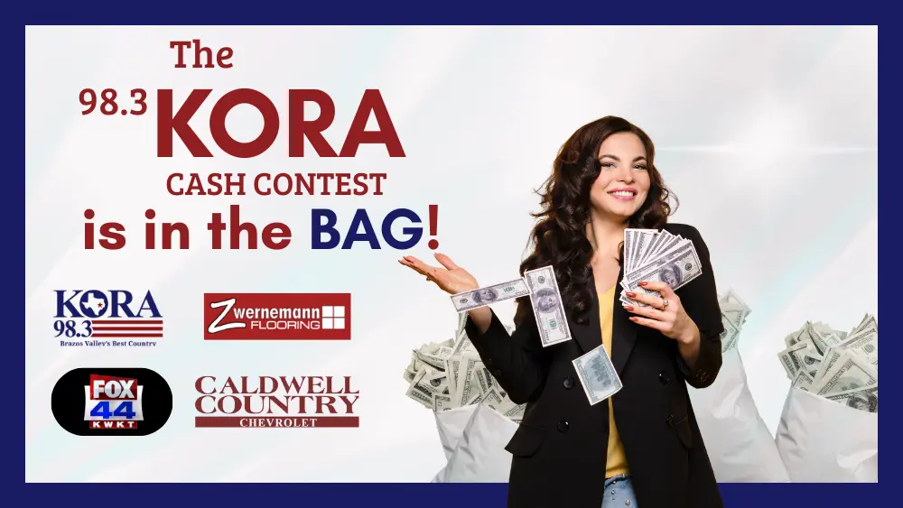 A woman holds a handful of cash while standing in front of bags of money.