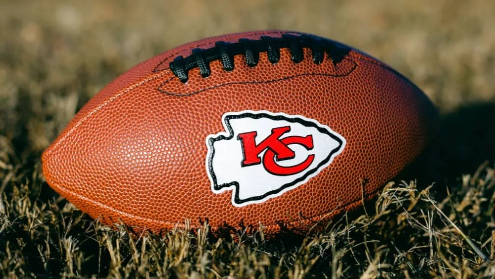 Kansas City Chiefs branded football laying on the grass^ with the arrowhead KC logo showing.