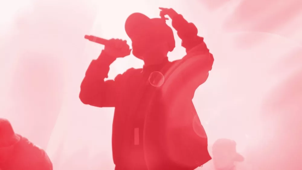 Silhouette of rap band performing on concert stage in bright red lights. Unrecognizable young rapper singing on concert