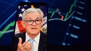 Federal Reserve (Fed) Chair Jerome Powell is visible. In the background^ an inflation rate chart is displayed.