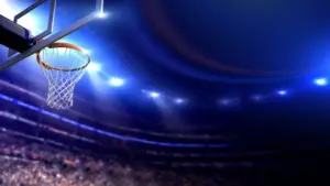 Basketball arena view of basketball hoop in dimmed arena^ crowd in silhouette^ lights turned on brightly