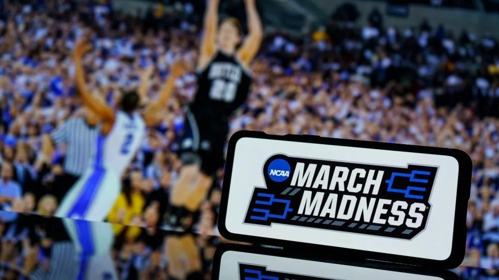 March madness logo on screen an basketball gameplay on TV screen in the background.