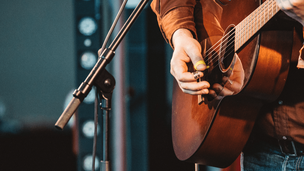 close up of hand of man playing guitar in concert on stage