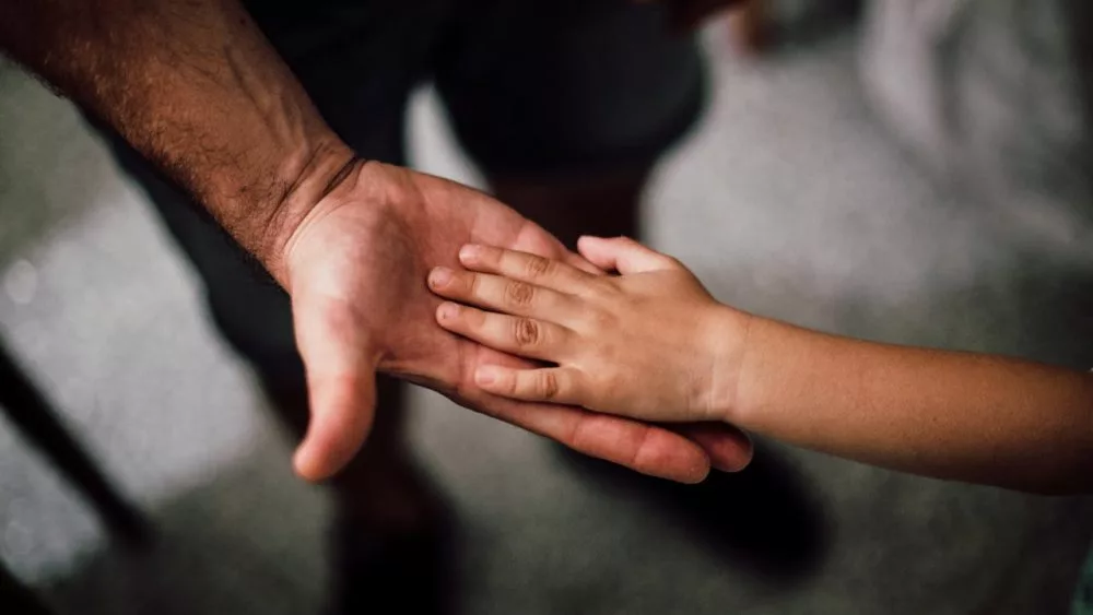 Photo of dad touching child's hand.