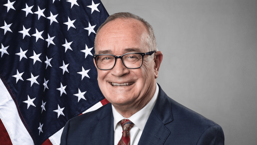 man in front of a grey wall and United States flag