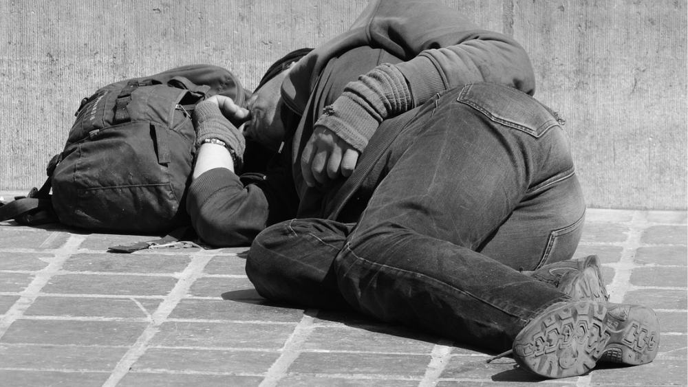 Image of a person sleeping on the ground with a backpack