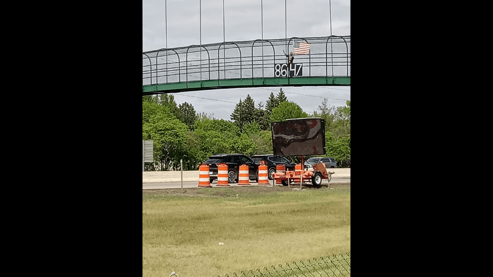 Image of Judd Hoff displaying an "8647" banner on Fargo's I-94 pedestrian bridge