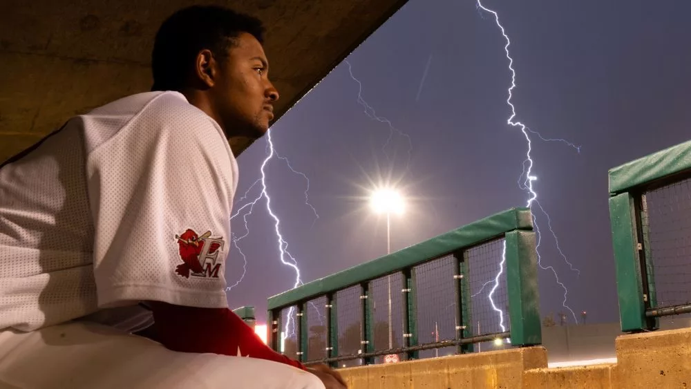 Player sitting on dugout bench with lightning in the background