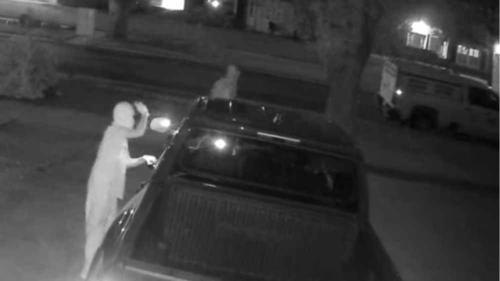 Screenshot of video showing two people peering into a parked pickup truck in the middle of the night