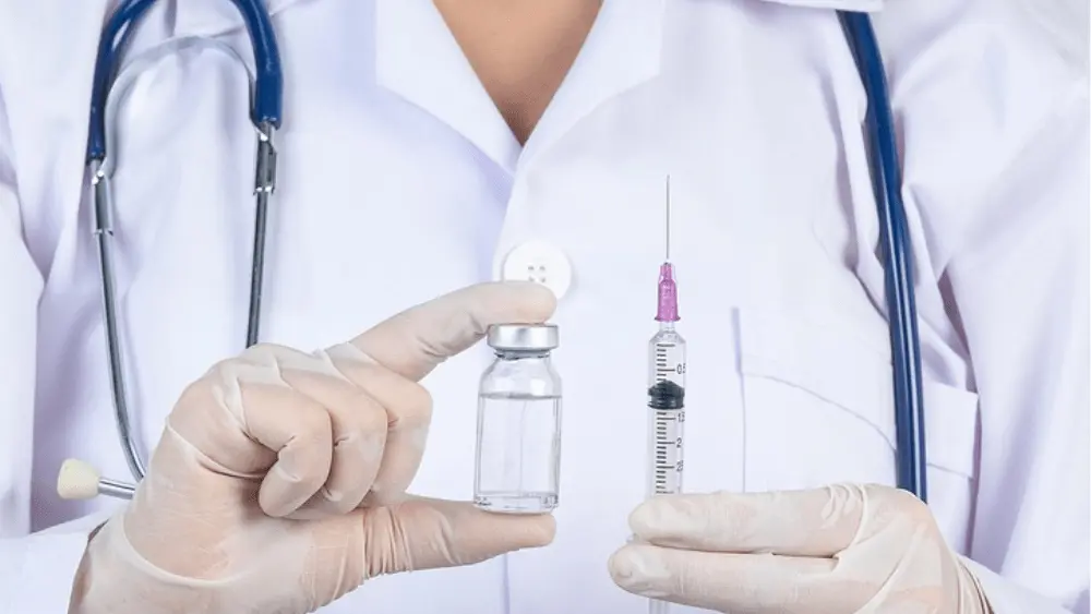 Image of health professional from neck down holding a hypodermic needle with serum