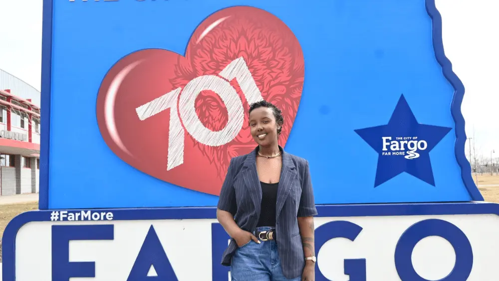 a woman in front of a sign that says 701^ Far More and Fargo